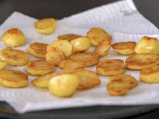Rodajas de patatas al horno, doradas y crujientes, reposando sobre papel absorbente. ¡Listas para disfrutar!