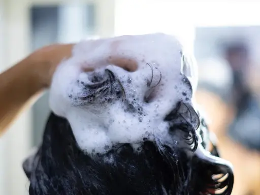 Mano che massaggia shampoo schiumoso sui capelli scuri, puliti o sporchi, per un momento di relax.