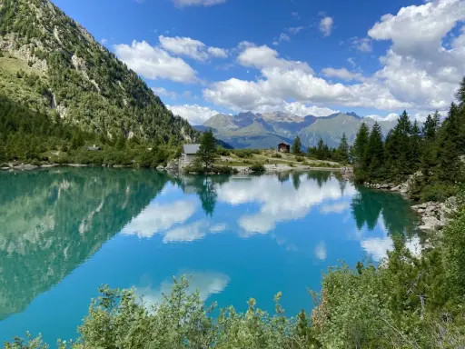 Lago alpino cristallino, perfetto per passeggiate in montagna Lombardia. Riflessi di cielo e montagne.