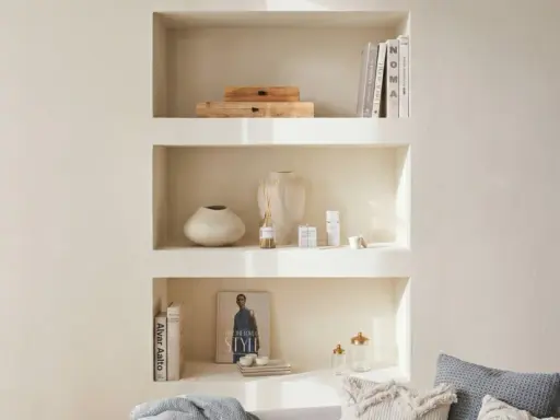Una nicchia nel muro del salotto, con libri, vasi e diffusore, crea un angolo accogliente e ordinato.