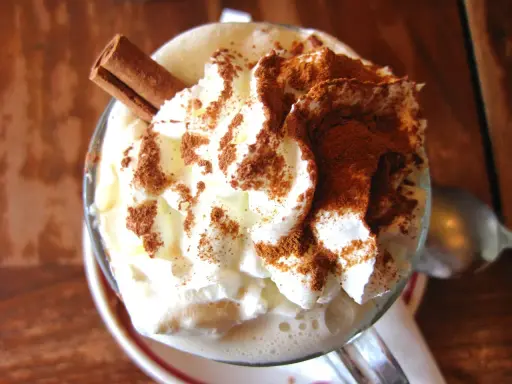 Un déliceux café liégeois recette : crème fouettée, cacao et bâton de cannelle dans un verre.
