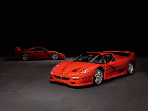 Zwei rote Ferraris, ein F50 und ein F40, stehen nebeneinander auf dunklem Grund.