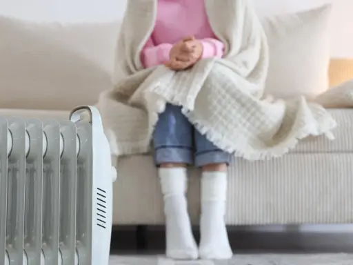 Radiador eléctrico junto a un sofá donde una persona se abriga. Una solución eficaz para los sistemas de calefacción del hogar.