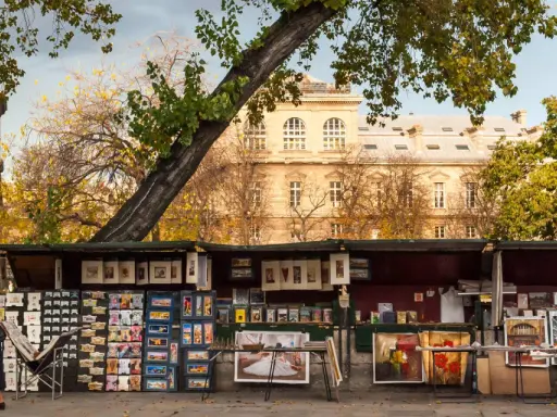 Ein Stand auf dem **Flohmarkt Paris** mit Postkarten, Büchern und Gemälden vor einem historischen Gebäude.