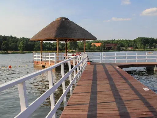 Drewniane molo nad zalewem Siemiatycze, z altaną krytą strzechą. W wodzie kąpie się osoba.