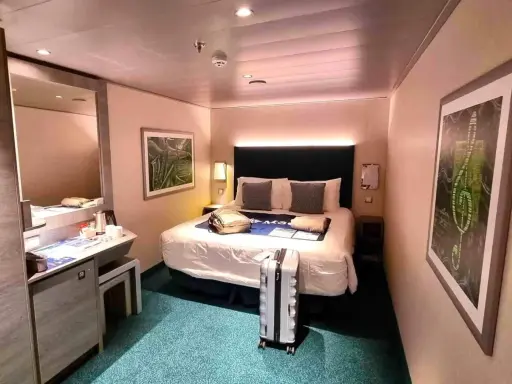 Interno di una royal caribbean cabine con letto matrimoniale, specchio, scrivania e valigia pronta per il viaggio.