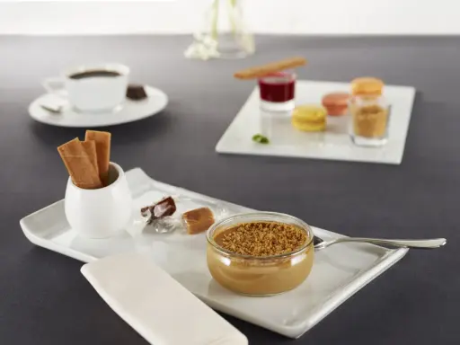 Un café gourmand avec diverses mignardises : verrine caramélisée, macarons, biscuits, chocolats. Idéal pour des recettes de mignardises pour café gourmand.