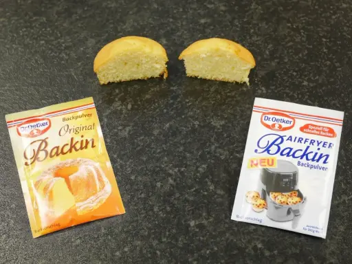 Zwei Päckchen Dr. Oetker Backin, einmal Original und einmal für den Airfryer, liegen neben zwei halbierten Küchlein. Perfekt für schnelles Backen mit Mehl und Backpulver.