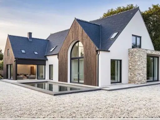 Une maison neuve en pierre et bois, avec une piscine rectangulaire devant.