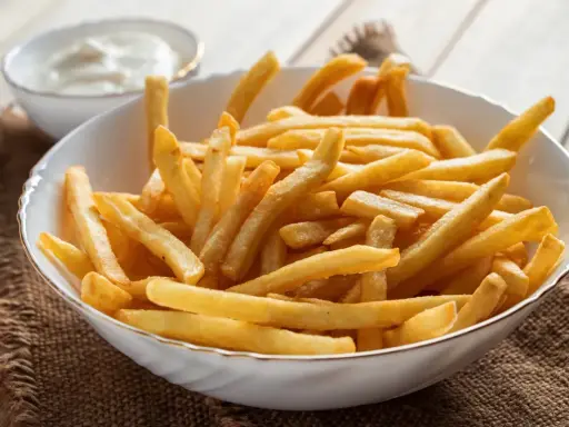 Chrupiące frytki z airfryer w białej misce, obok sos. Idealna przekąska na szybki obiad.