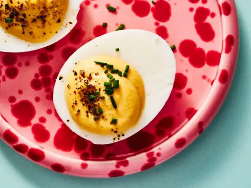 Deviled eggs deutsch: halbe hartgekochte Eier mit cremiger Füllung, bestreut mit Schnittlauch und Gewürzen, auf einem pinkfarbenen Teller mit roten Tupfen.