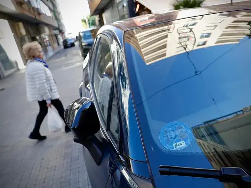 Una mujer cruza la calle mientras un coche eléctrico, con distintivo DGT, espera. Los coches eléctricos pagan zona azul.