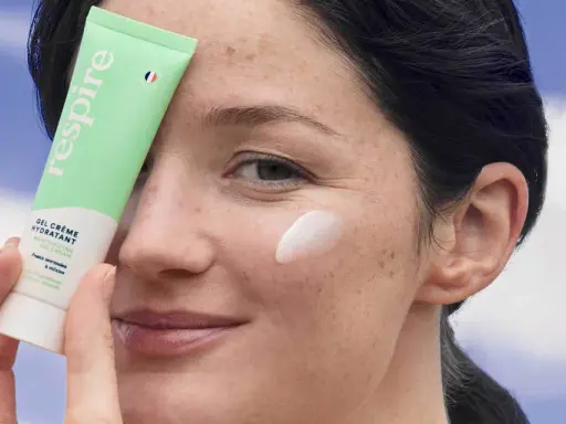 Une femme applique une crème hydratante sur sa joue. Une solution pour comment hydrater sa peau très sèche.
