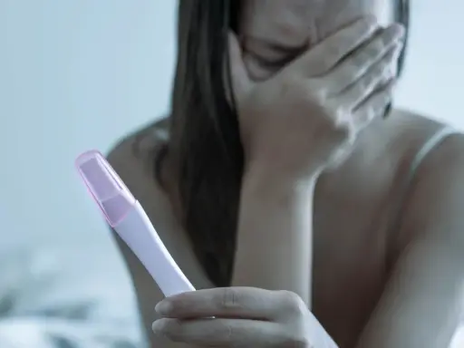 Dziewczyna z zakrytą twarzą trzyma test ciążowy, przeżywając strach przed ciążą po stosunku.
