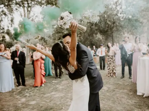 Novios besándose con humo verde, ¡ideas para una boda diferente! Invitados aplauden y celebran.