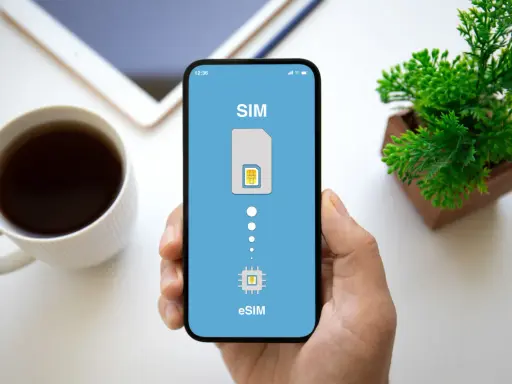 Dłoń trzyma smartfon z ekranem pokazującym proces aktywacji eSIM. Obok kubek kawy i roślinka.