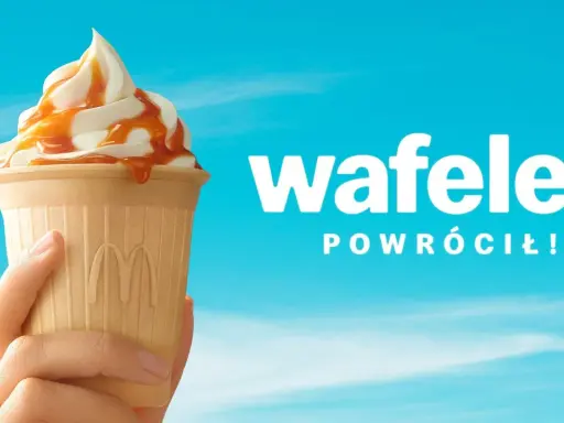 Lody McDonald's w wafelku z polewą karmelową, trzymane w dłoni na tle błękitnego nieba.