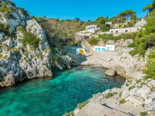 Baia incantevole con acque cristalline, perfetta per un itinerario Puglia 3 giorni. Case bianche e rocce a picco sul mare.