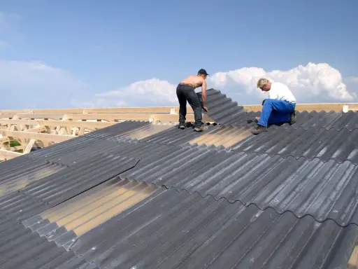 Zwei Handwerker sanieren ein Eternitdach. Die Kosten für die Sanierung eines Eternitdachs sind oft eine wichtige Überlegung.