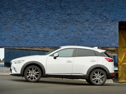Biała Mazda CX-3 na tle niebieskiej ściany. Sprawdź aktualną mazda cx3 cena i wybierz swój wymarzony samochód.