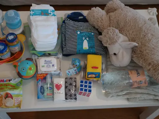 Zestaw zawiera przekąski do samolotu dla dziecka: chrupki, słoiczki, pieluchy, chusteczki, butelki, ubranko i pluszaka.