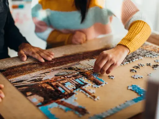 Dwie osoby składają puzzle, tworząc obraz. To dowód na to, że najlepsi producenci puzzli tworzą dzieła, które łączą ludzi.