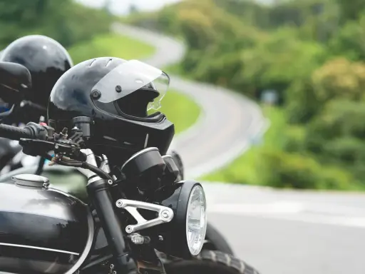 Gotowe na przygodę? Zastanawiasz się nad prawem jazdy na motor i wiekiem? Dwa kaski czekają na motocyklistów na krętej drodze.