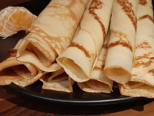 Crêpes à la bière roulées, dorées et légères, servies sur une assiette noire avec un quartier d'orange. Un délice !