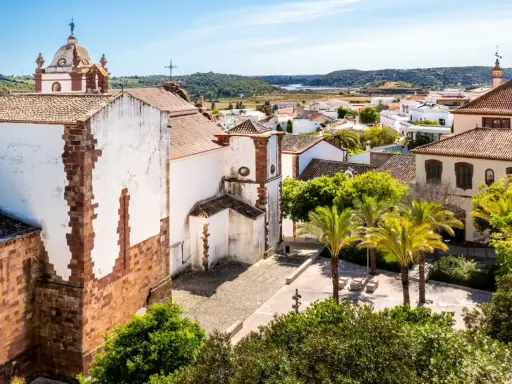 Blick über die weißen Häuser und Palmen von Silves, Portugal, mit einer Kirche im Vordergrund.