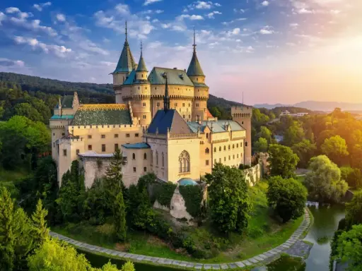 Bajkowy zamek otoczony zielenią, idealne miejsce na nocleg w zamku. Słońce zachodzi nad wzgórzami, tworząc magiczną atmosferę.