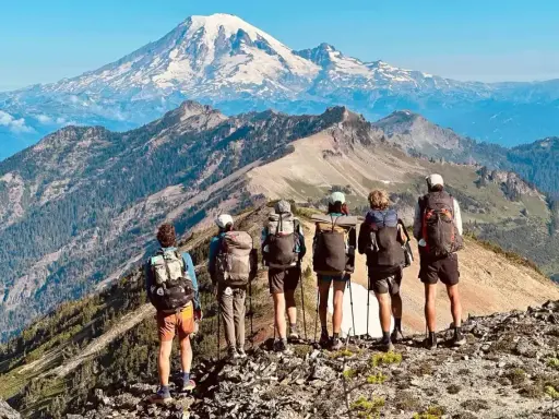 Sześcioro turystów z plecakami na grani, podziwiających majestatyczny szczyt góry na tle błękitnego nieba. To piękny widok z Pacific Crest Trail.
