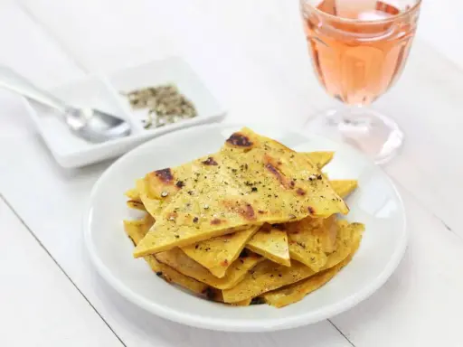 Une assiette de socca à la poêle, coupée en triangles et saupoudrée de poivre, à côté d'un verre de rosé.