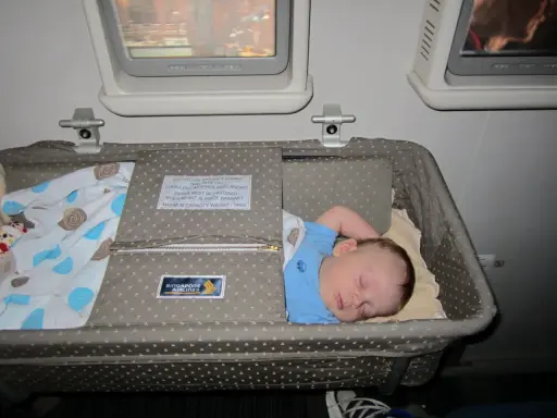 Śpiące dziecko w wózku dla dziecka Singapore Airlines podczas lotu. Wygodny enter air wózek dla dziecka zapewnia spokojny sen maluchowi.