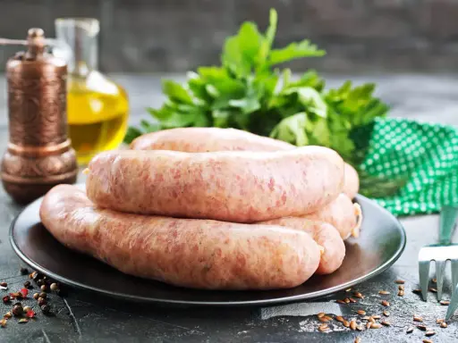 Świeża kiełbasa na talerzu, obok przyprawy i ziół. Zastanawiasz się, jak długo można mrozić kiełbasę?
