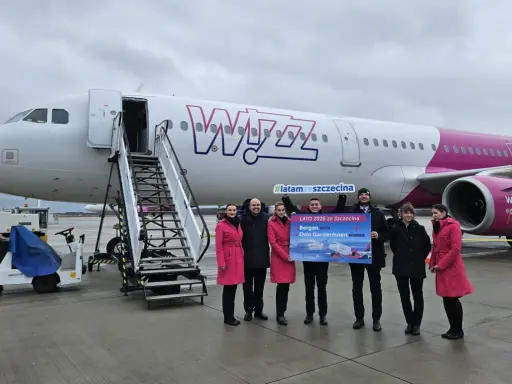 Grupa osób pozuje przed samolotem Wizz Air, trzymając tablicę z informacją o nowych trasach, w tym lotach Szczecin-Bergen.
