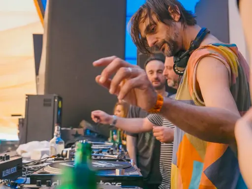DJ Villa Lobos, con cuffie al collo, mixa musica con passione. Dietro di lui, il pubblico attende il ritmo.