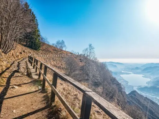Sentiero sul monte Coltignone con vista panoramica su un lago e montagne nebbiose.