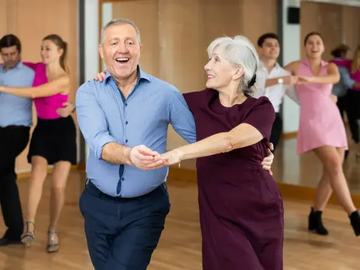 Uśmiechnięta para seniorów uczy się, jak tańczyć na 3, w tle inne pary.