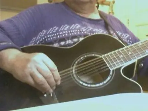 Main d'un musicien ajustant l'accordage 12 cordes d'une guitare acoustique noire.