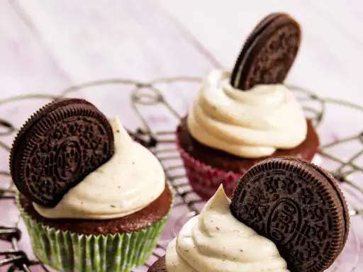 Drei leckere Oreo Muffins mit cremiger Glasur und einem ganzen Oreo-Keks darauf, auf einem Gitter.