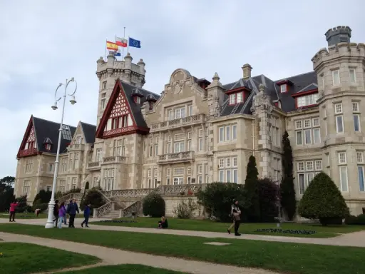 Palacio de la Magdalena en Santander, con banderas ondeando en la torre. Turistas pasean por los jardines de esta joya arquitectónica.