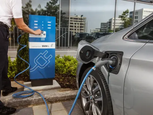 Un uomo collega un'auto elettrica a una colonnina di ricarica BMW i. Un passo verso il calcolo risparmio auto elettrica.