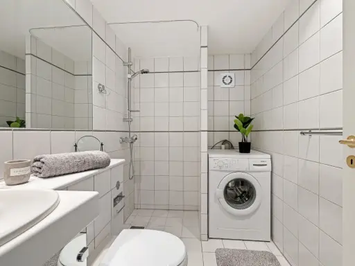 Baño con lavadora, ducha y un extractor de aire en la habitación para mantener la frescura.