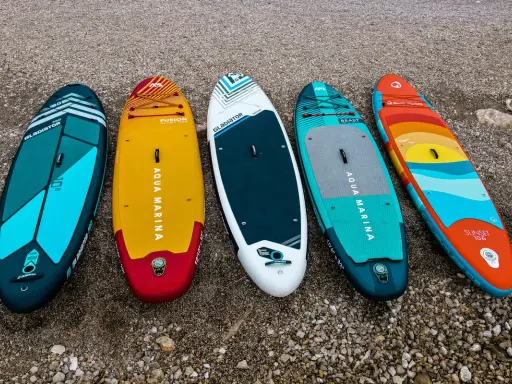 Pięć kolorowych desek z wiosłem leży na plaży. Gotowe na przygodę na wodzie!
