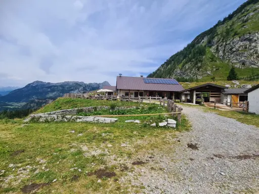 Malga Tuglia, un rifugio alpino con pannelli solari, immerso nel verde con montagne sullo sfondo.