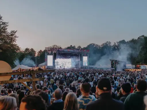 Stor publik vid Rosendal Garden Party. En stor scen med artister och ljus. Rök och träd i bakgrunden.
