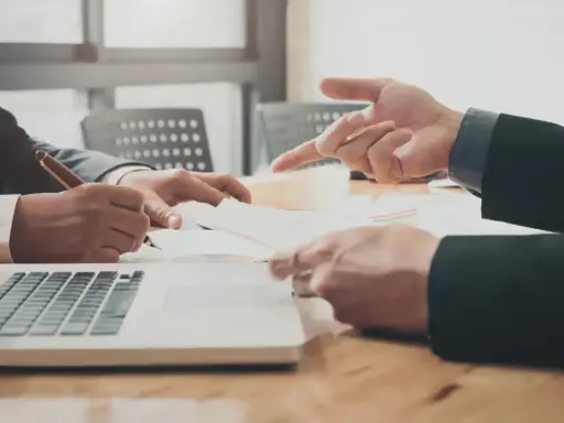 Dwóch mężczyzn w garniturach analizuje dokumenty przy laptopie. Rozpoczynają własną działalność, omawiając strategię.
