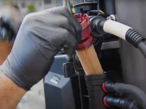 Main d'un mécanicien en gant noir retirant un filtre à gasoil encrassé, conséquence d'un mauvais entretien.