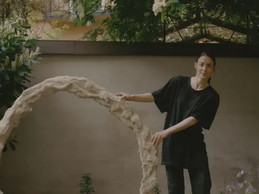 Kajsa Melchior står vid en skulptur i en trädgård.