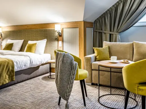 Przytulny pokój hotelowy z dwoma łóżkami, kanapą i fotelami. Idealne miejsce na relaks po podróży.